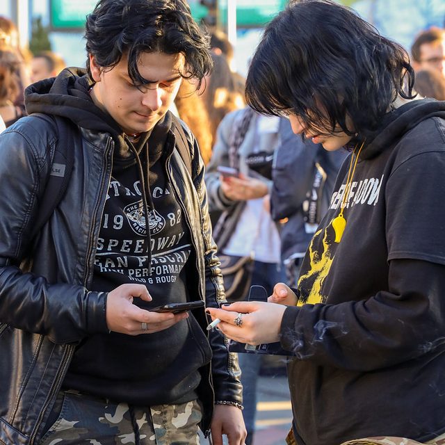 Two friends looking at their phones on a busy street