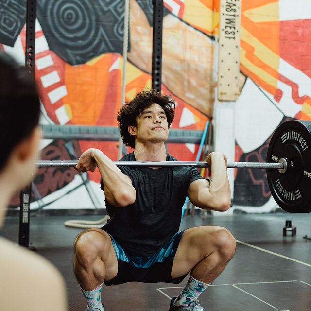 A man lifting a barbell in a busy gym